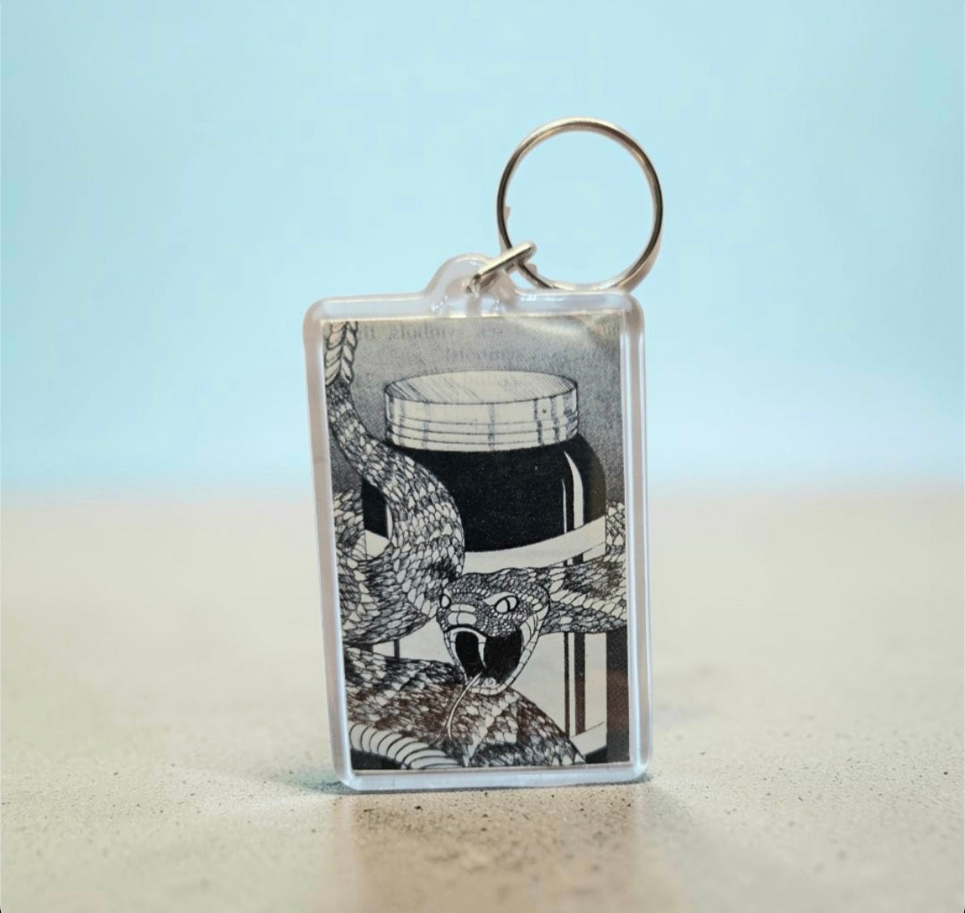 Keychain featuring a black-and-white graphic illustration of an aggressive, striking snake coiled around a glass jar
